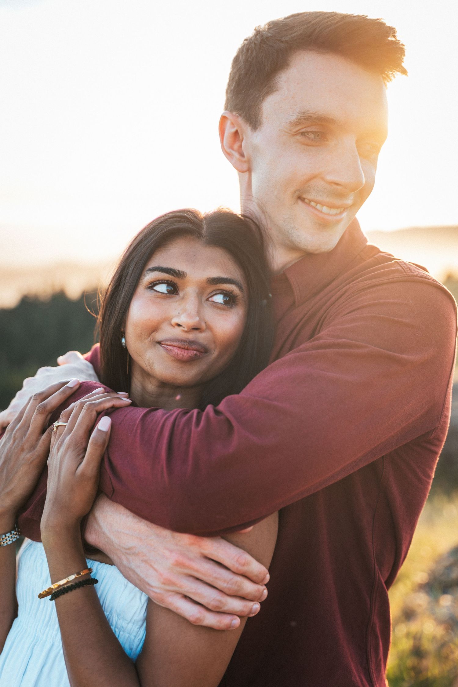Interracial couple embracing warmly at golden hour with scenic hills in the background.