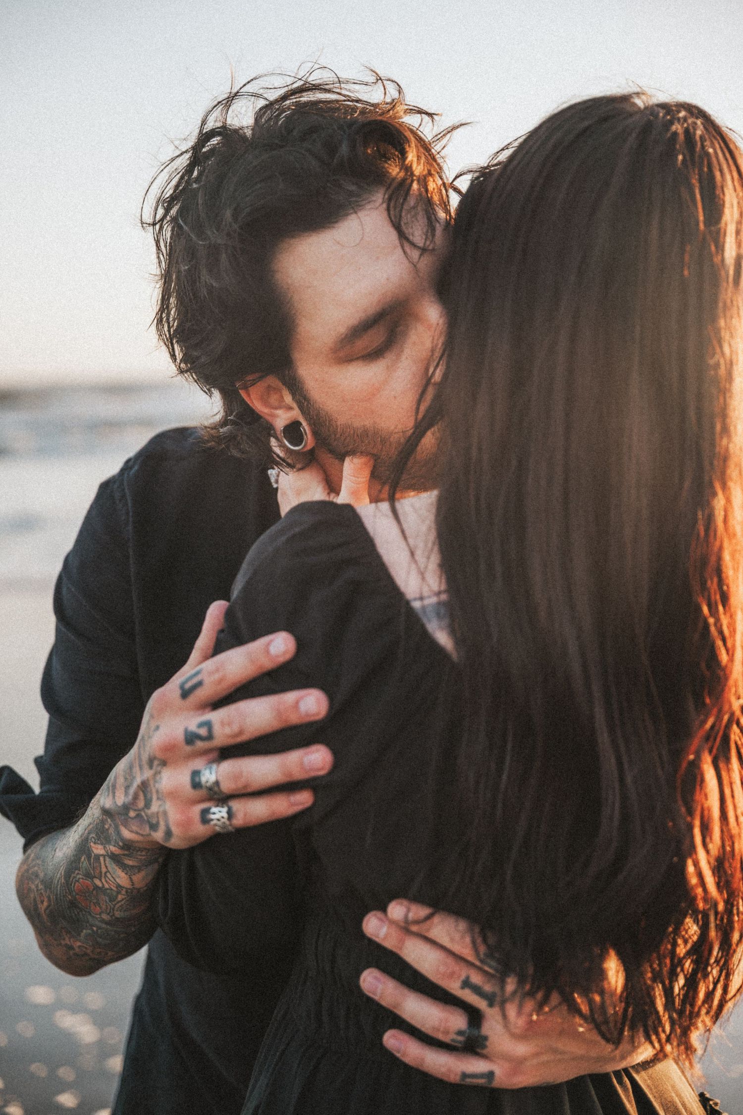 Tattooed couple kissing intimately on a beach at golden hour sunset.