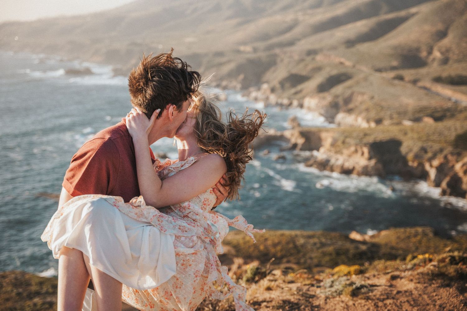 Couple sharing a romantic kiss on a scenic coastal cliff overlooking the ocean at Big Sur, California.