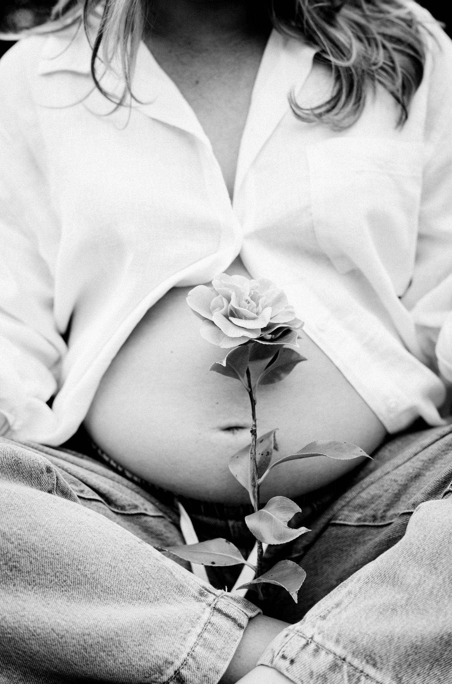 Black and white photo of pregnant woman in white shirt holding a rose against her bare baby bump.