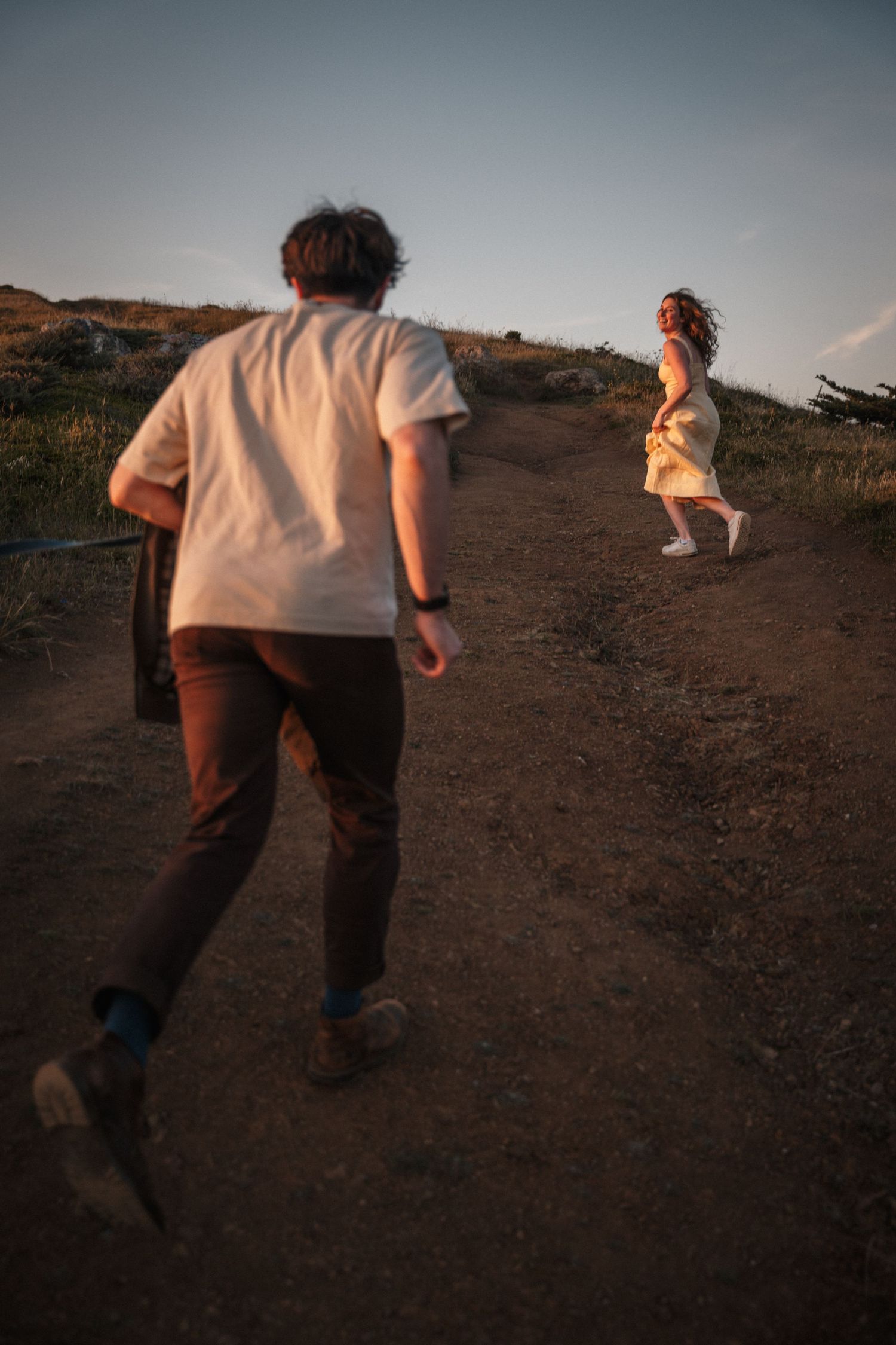 Couple running together on a dirt trail at sunset with ocean views.