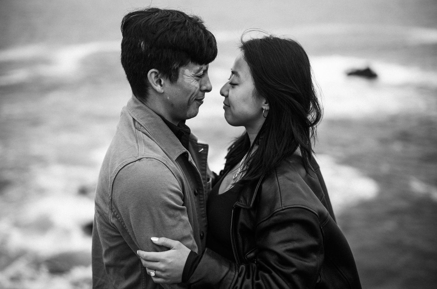 Black and white photo of couple sharing intimate moment near ocean shoreline.