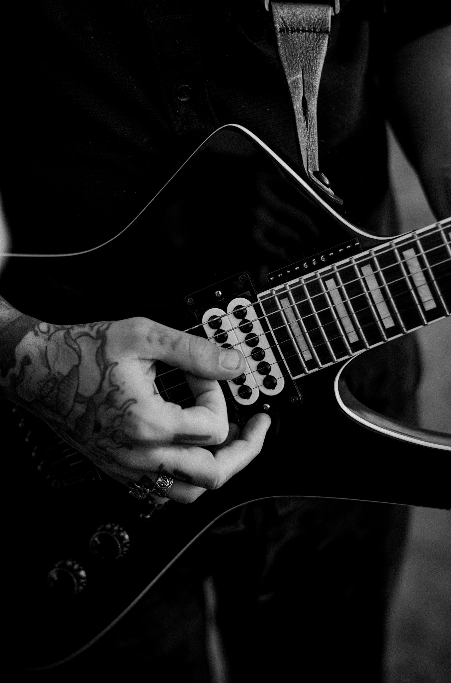 Tattooed hands playing black electric guitar close-up in black and white.