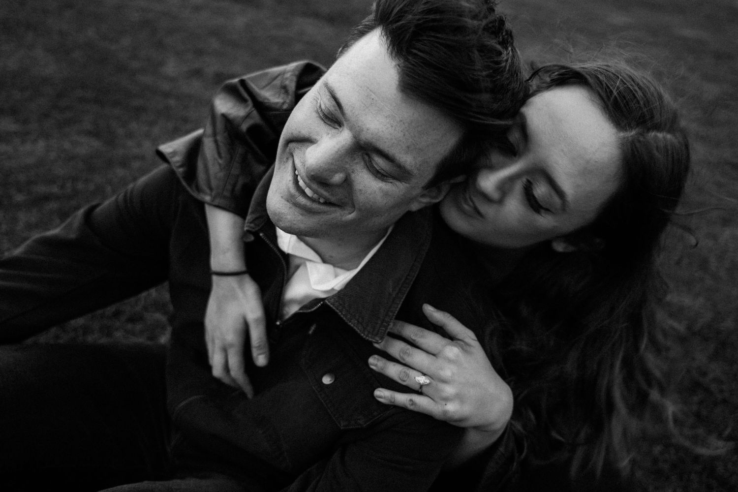 Black and white photo of a couple laughing and cuddling together on grass.