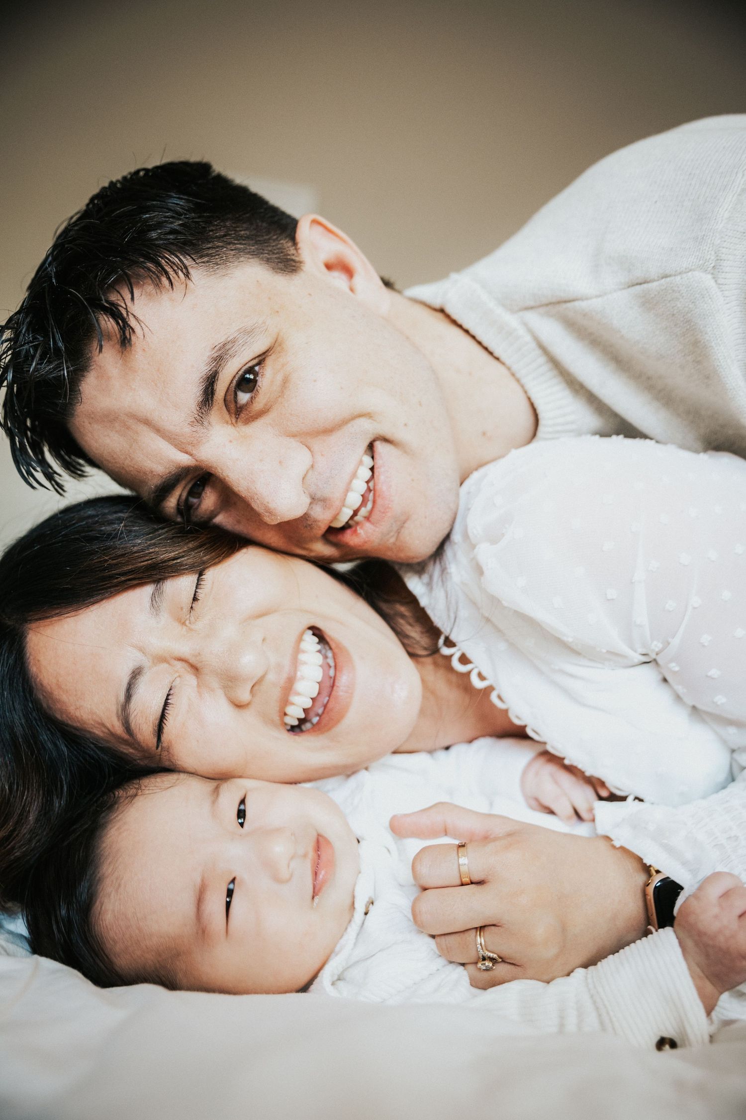 Happy family of three lying together, parents smiling with their baby in a warm, cozy portrait.
