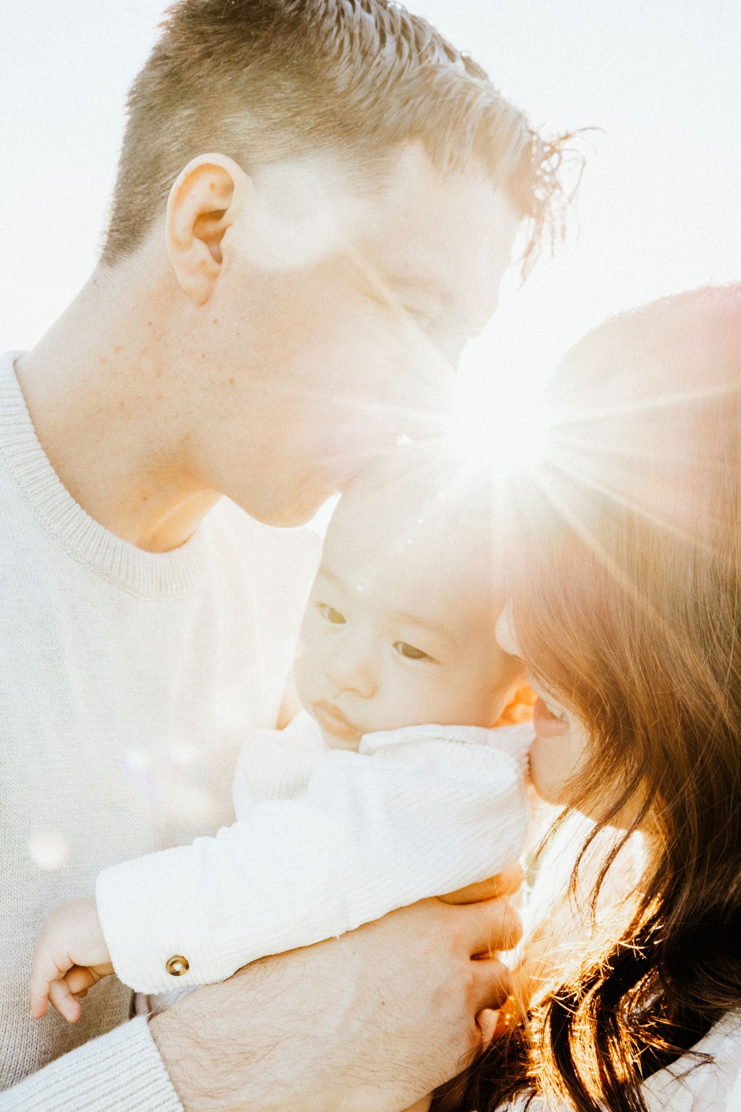 Couple holding baby in bright sunlight with warm lens flare in intimate family portrait.