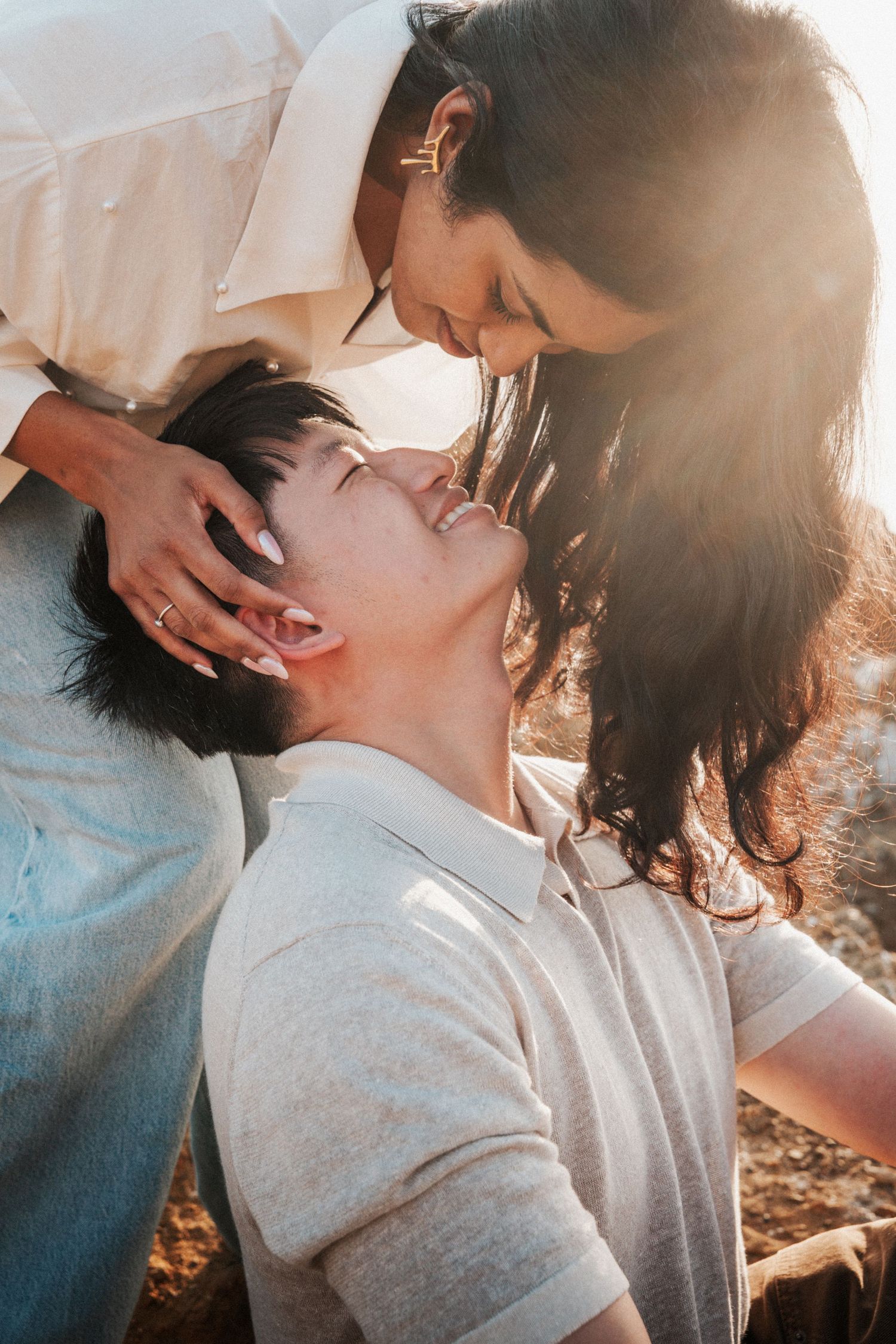 Couple sharing a romantic moment in golden sunlight, woman tenderly holding man's face as they lean in for a kiss.