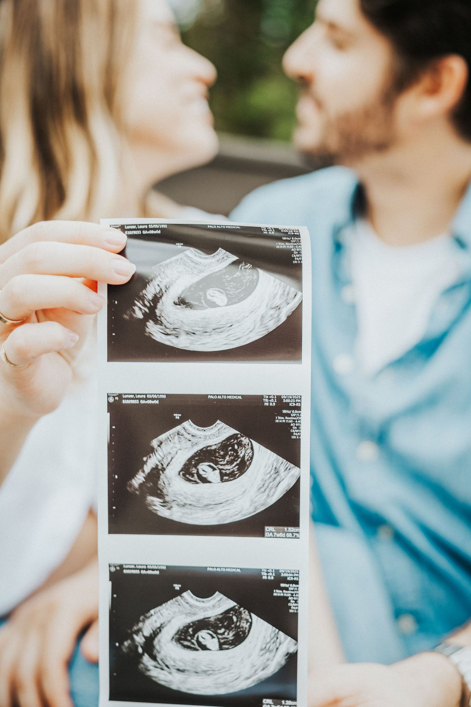 Couple holding ultrasound photos while sharing a tender moment outdoors, celebrating their pregnancy announcement.