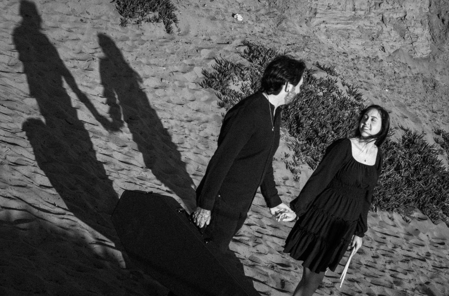 Black and white photo of a couple holding hands outdoors, with dramatic shadows cast on a stone path.