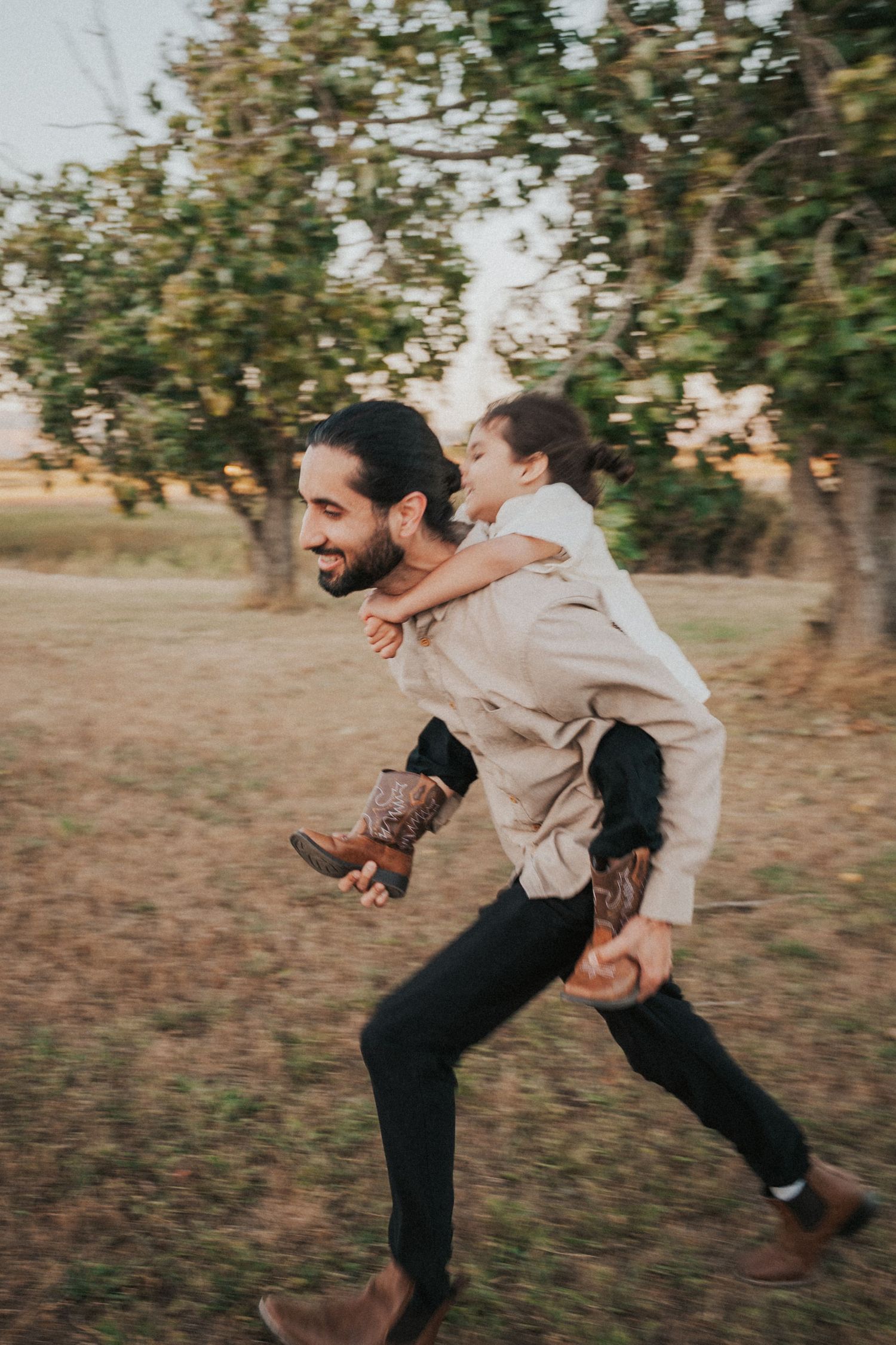 Laughing father giving his son a piggyback ride in a green outdoor setting.