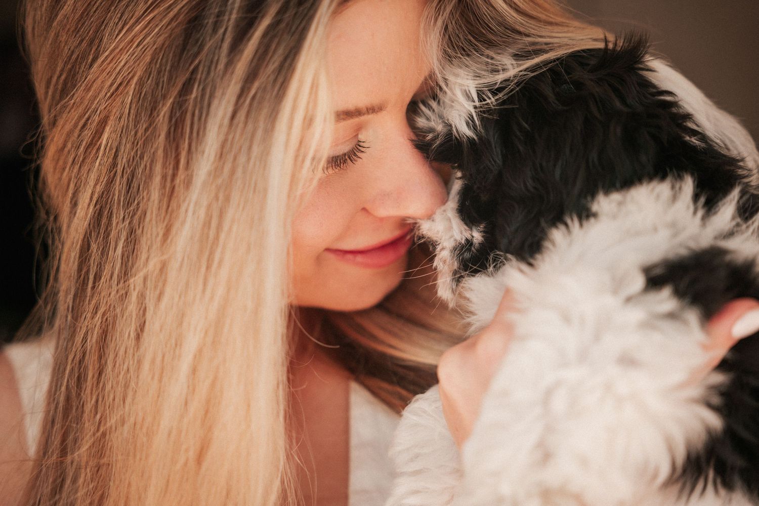 A blonde woman shares a tender moment nuzzling a black and white fluffy puppy.