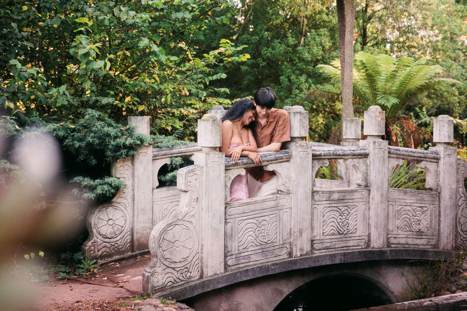 Couple leaning together on a decorative stone bridge admiring the view in a serene garden.