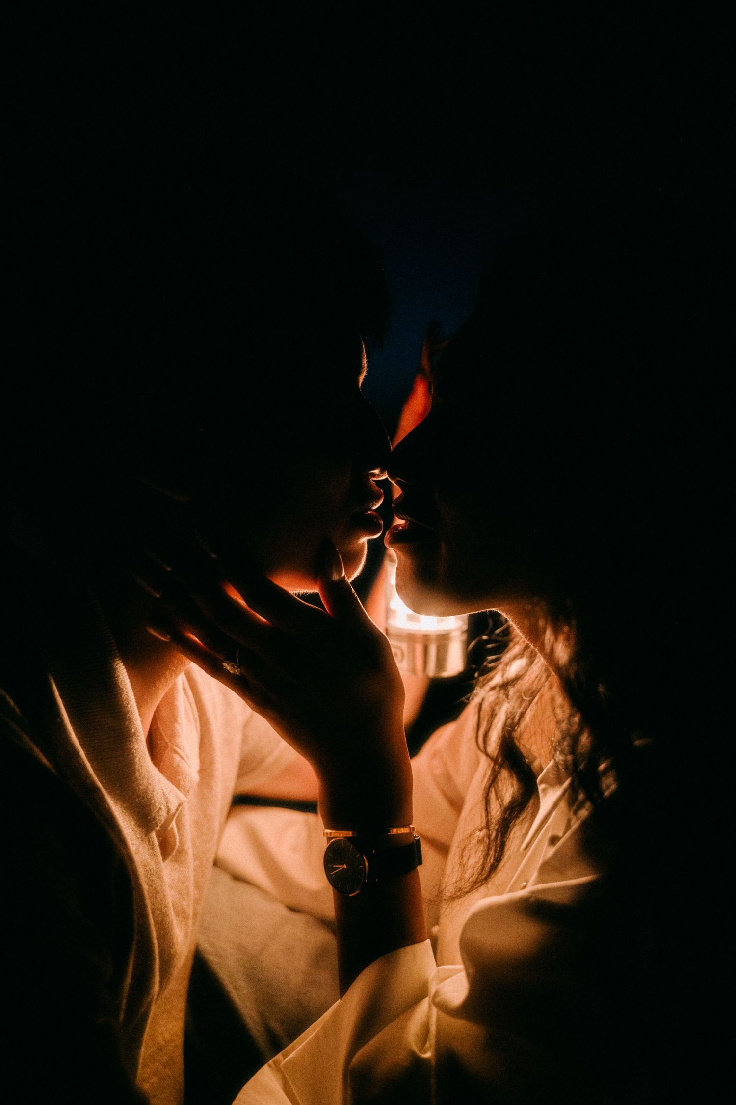 Dramatic dark silhouette of a couple about to kiss illuminated by warm candlelight glow.