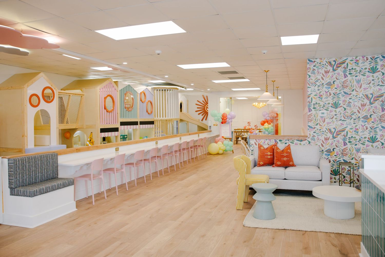 Spacious children's party venue with pastel play structures, pink bar seating, and decorative floral wallpaper.