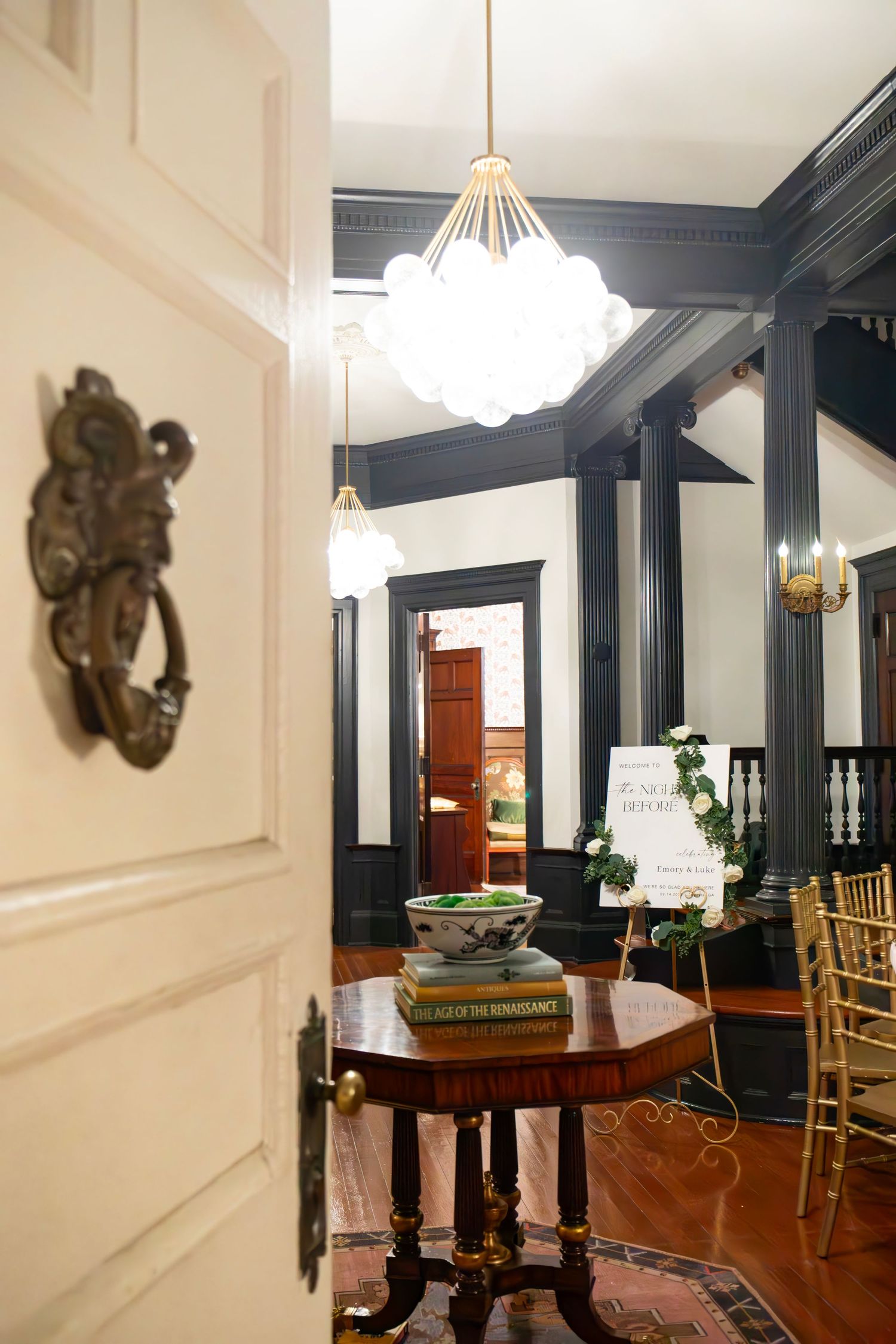 Elegant historic venue foyer with ornate door knocker, globe chandelier, and classic dark wood architectural details.