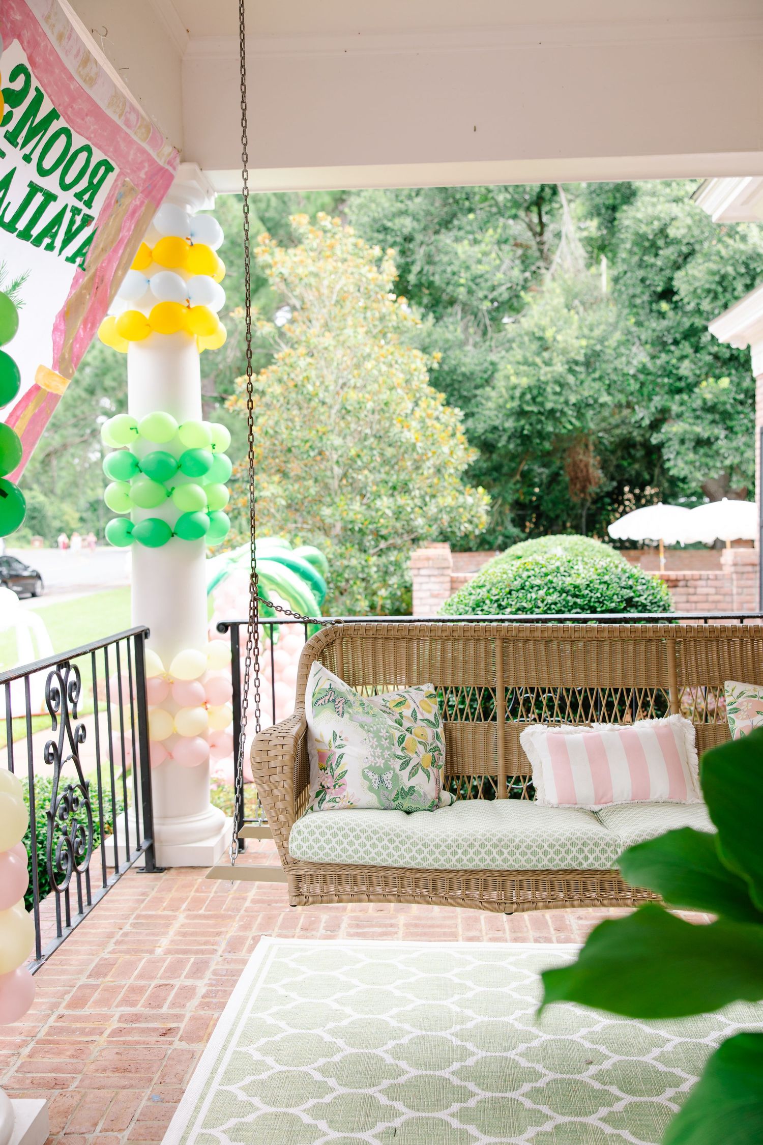 Charming porch with wicker swing, colorful balloon column, and pink striped banner for a Phi Mu sorority event.