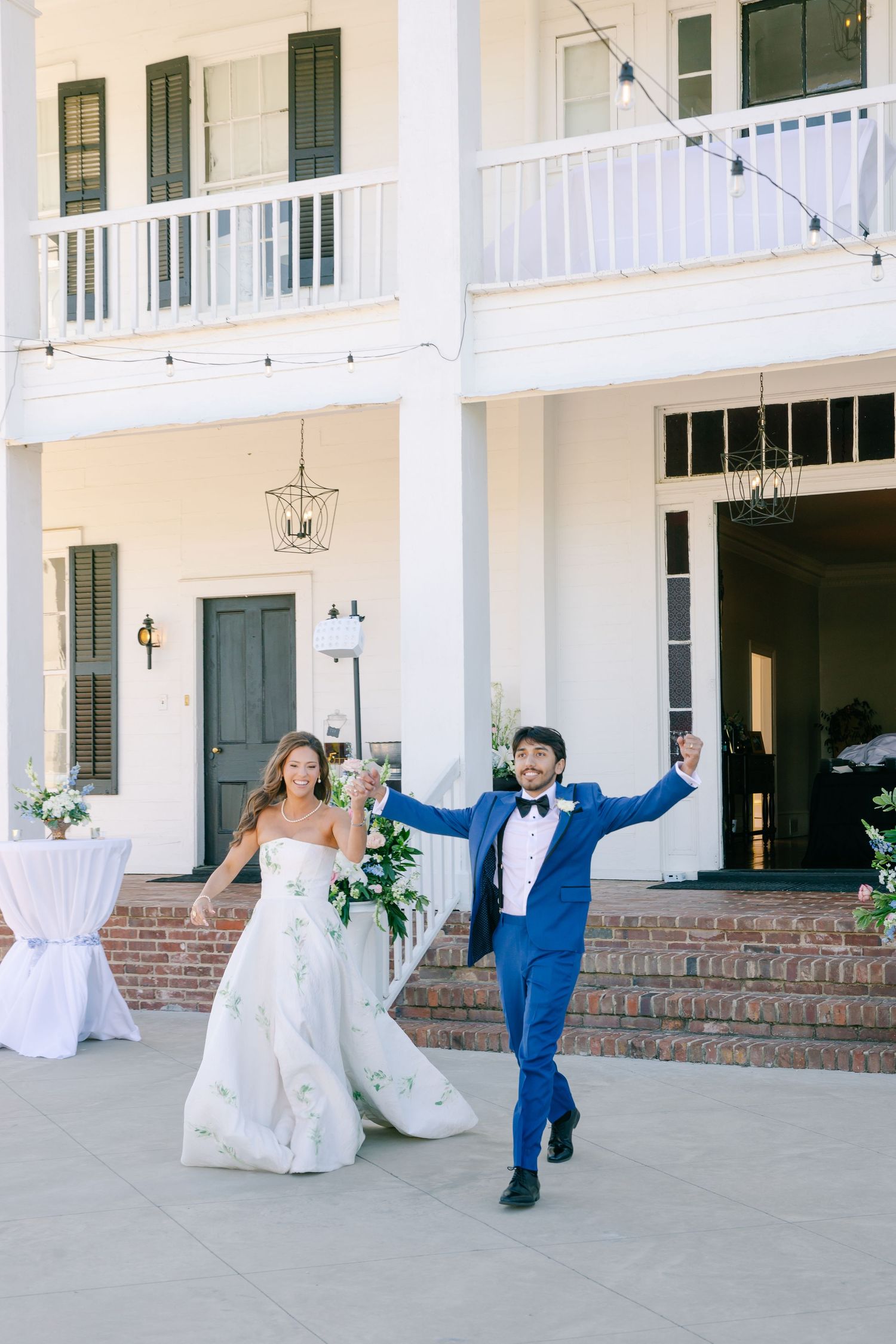 Bride and groom celebrating joyfully outside grand white colonial wedding venue.