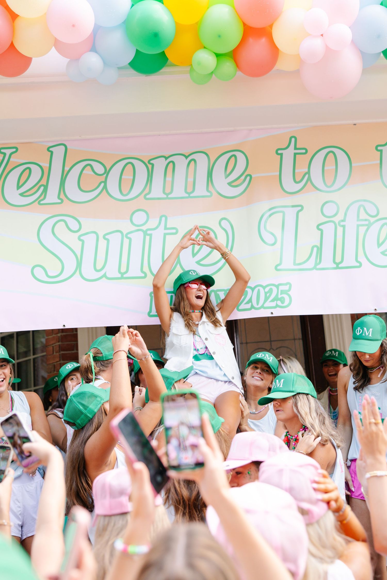 Phi Mu sorority member celebrates atop crowd at Welcome to the Suite Life 2025 bid day banner event.