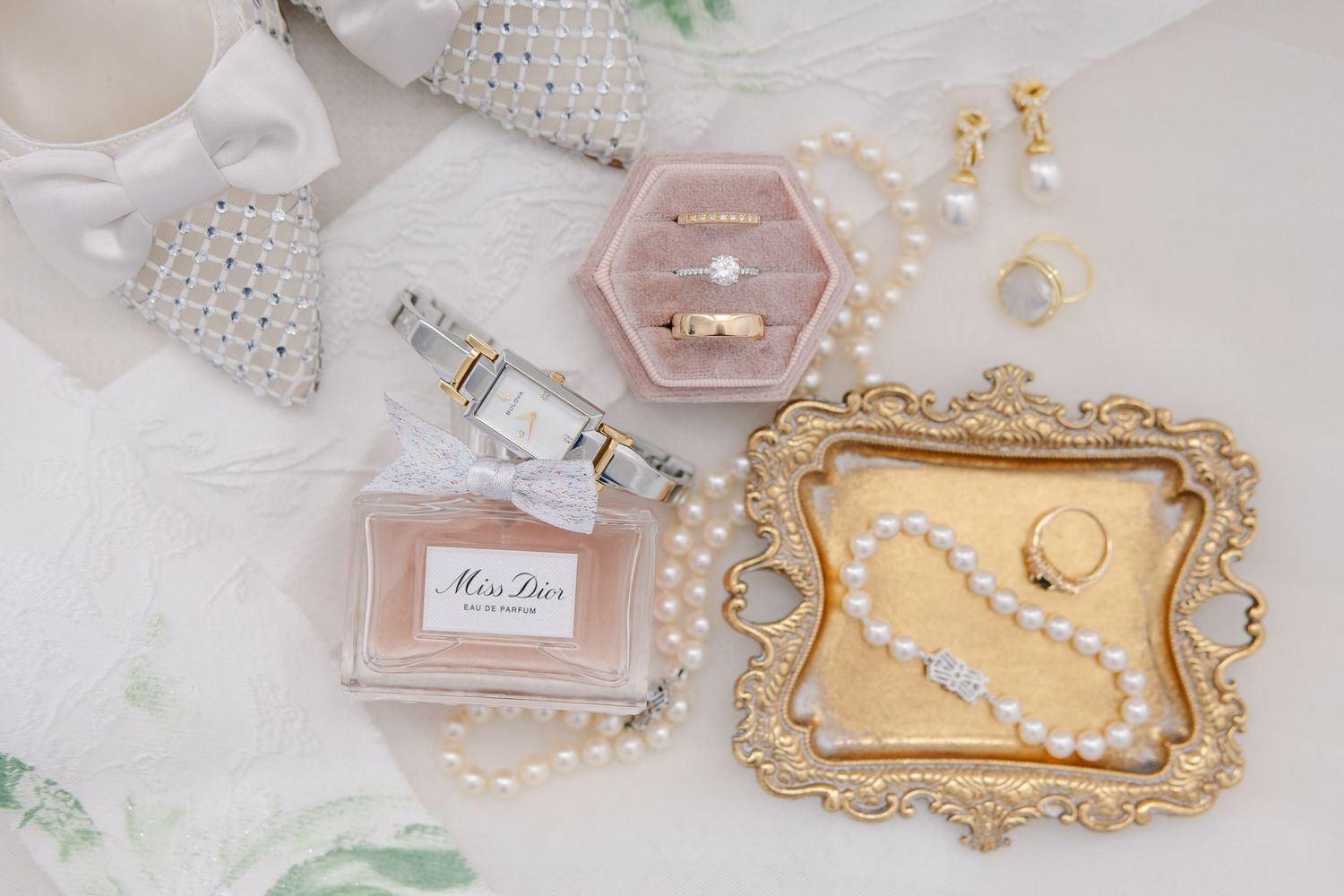 Bridal flat lay featuring Miss Dior perfume, pearl jewelry, gold tray, watch, and ring box.