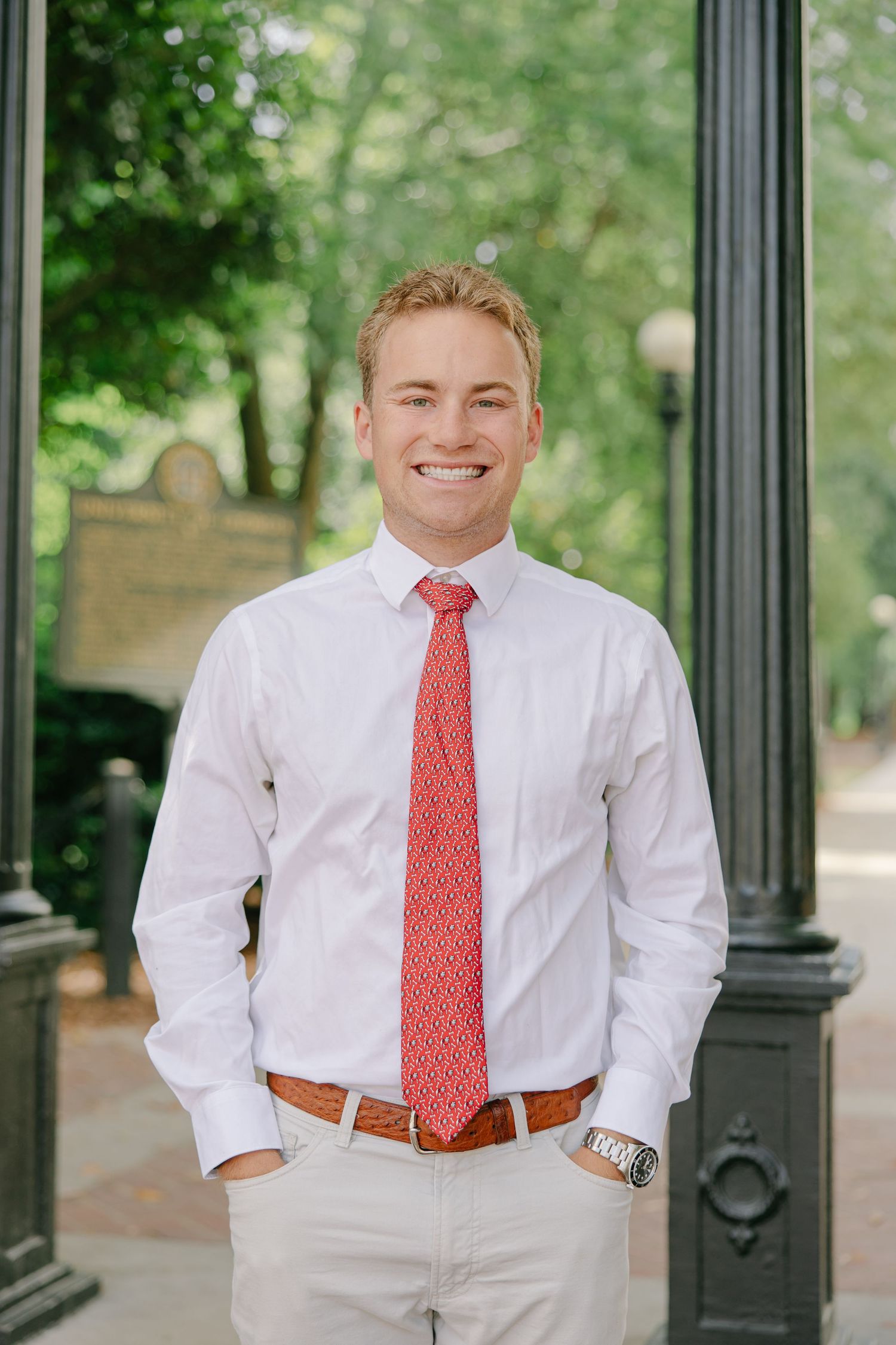 Smiling young man in white shirt and red tie standing outdoors.