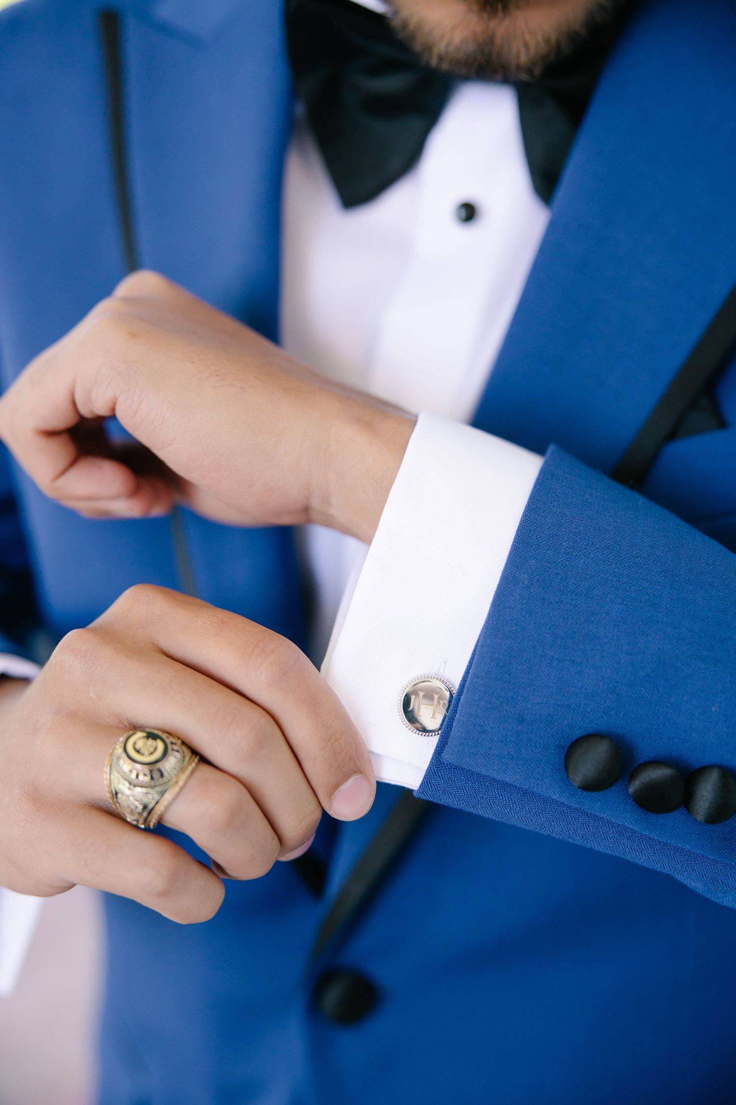 Close-up of groom in blue tuxedo adjusting cufflinks wearing ornate gold signet ring.