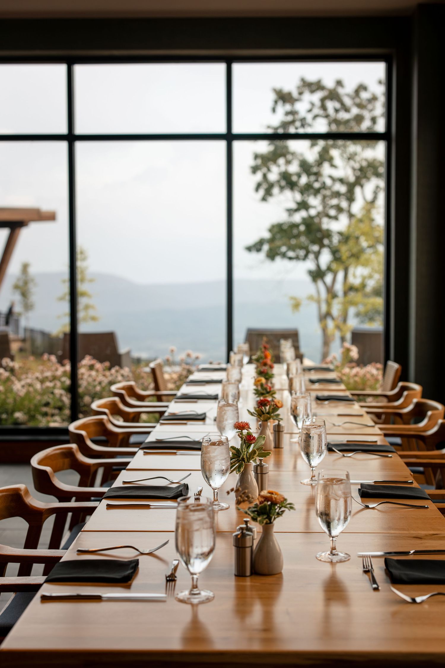 Elegant restaurant dining room with long wooden tables set for a group meal with mountain views.