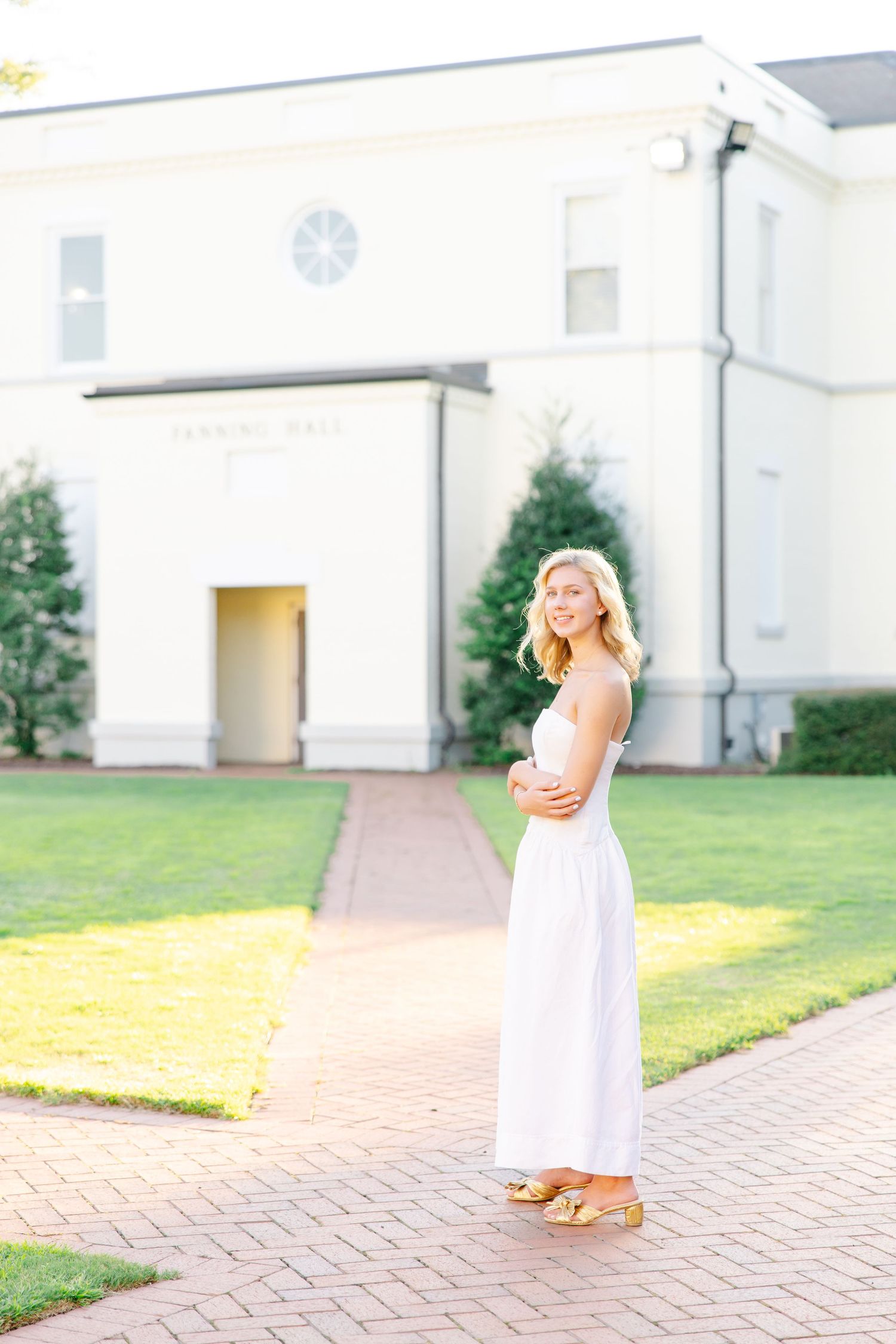 Smiling blonde woman in white dress posing on brick path outside Fanning Hall building.