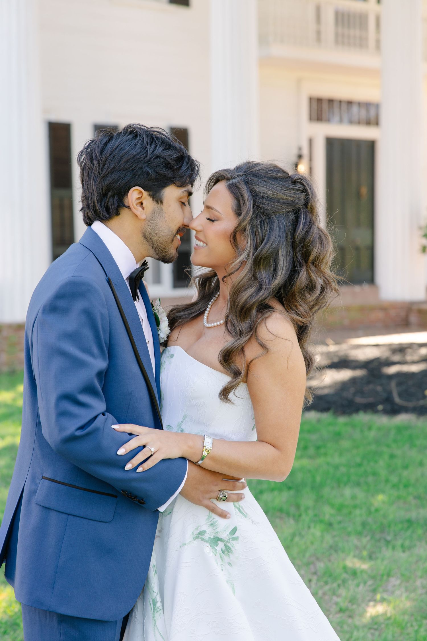 Bride and groom share a romantic almost-kiss moment outdoors near white columns of an elegant Southern estate venue.