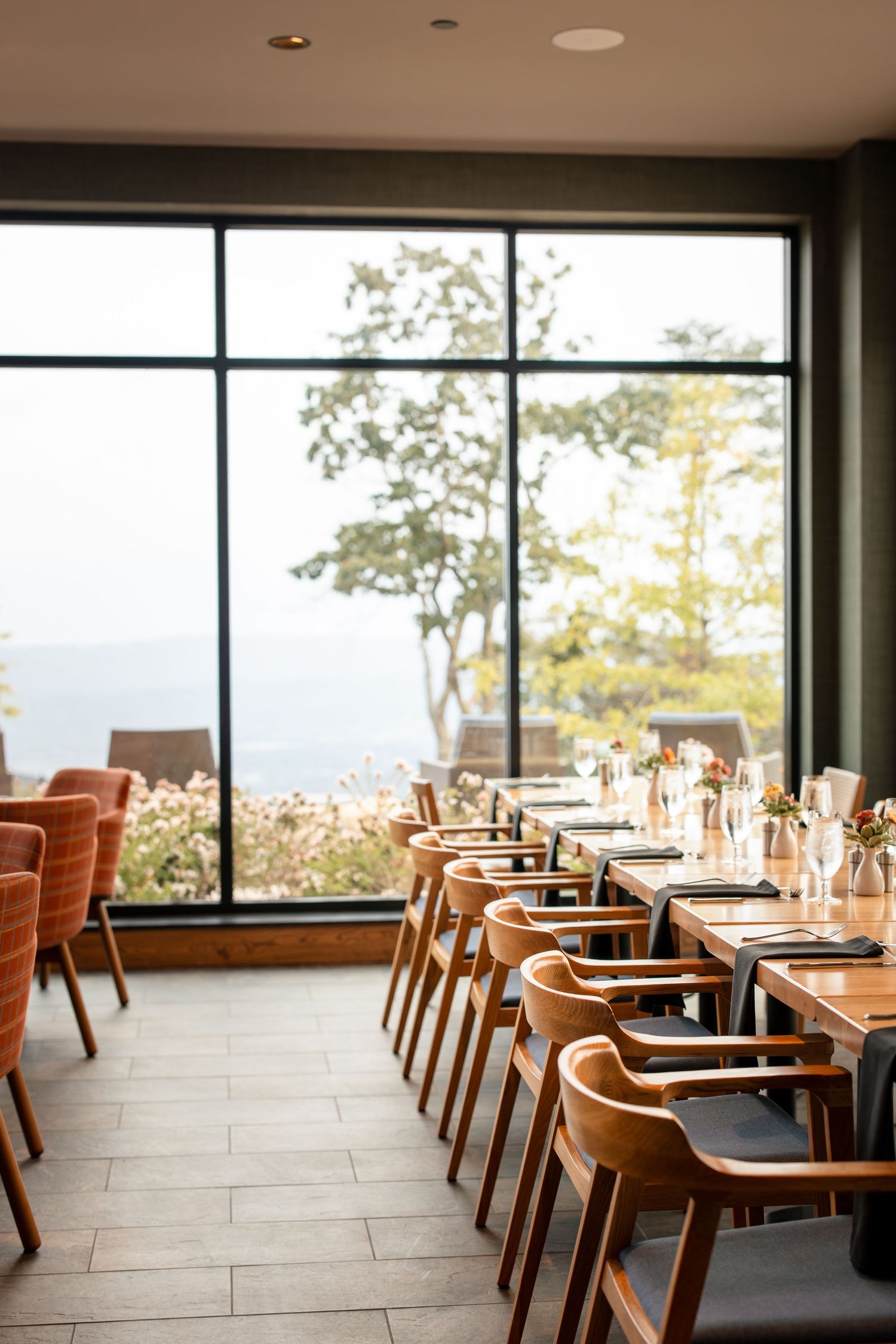 Modern restaurant interior with wooden chairs and large windows overlooking mountain scenery.