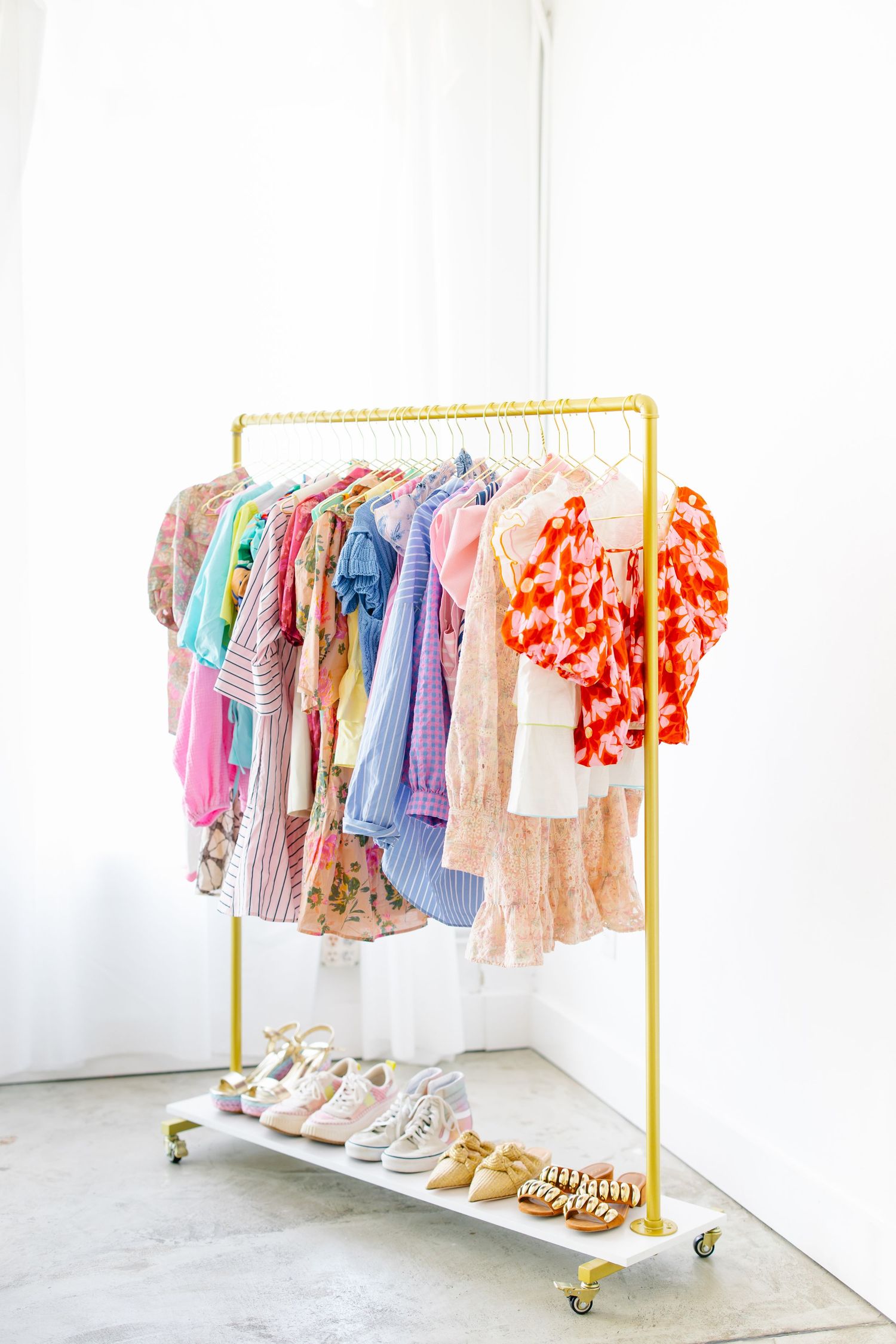 Colorful women's clothing rack with rainbow of dresses and tops on gold rolling rack with shoes displayed below.