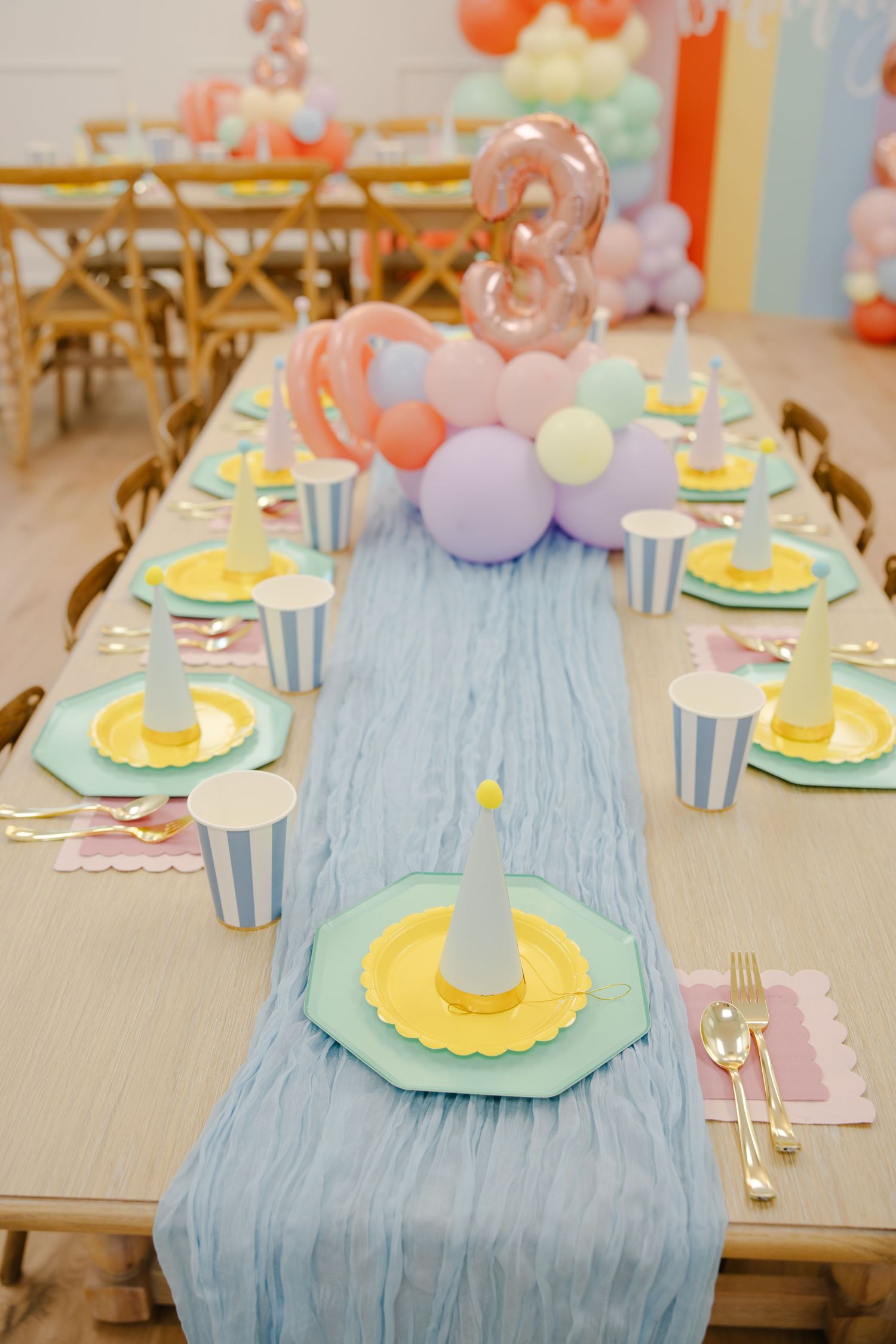 Long birthday party table with blue table runner, mint and yellow plates, striped cups, and balloon centerpiece.
