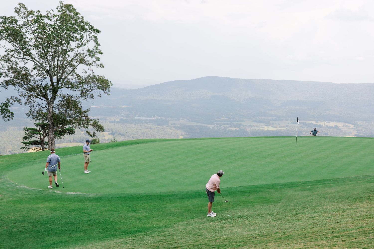 Golfers playing on a lush green mountain golf course with scenic valley views.