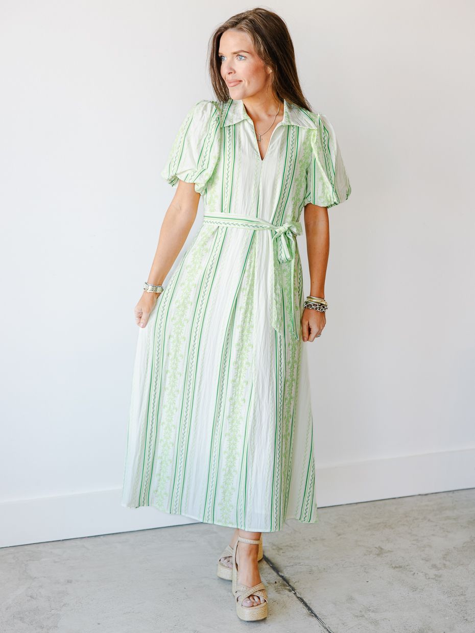 Woman wearing a green and white striped midi dress with flutter sleeves and a tie waist, paired with espadrille wedges.