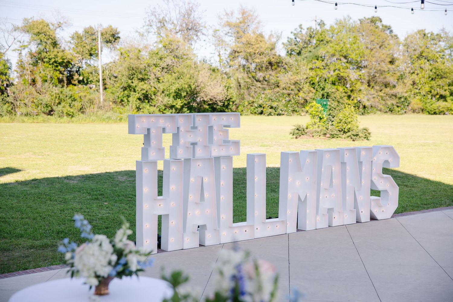 Large white marquee letter sign reading The Hallmans at outdoor wedding reception.