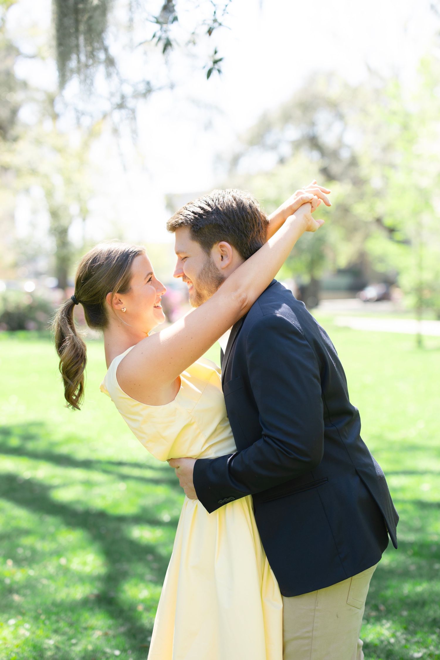 Happy couple dancing and embracing outdoors in a sunny green park, woman in yellow dress.