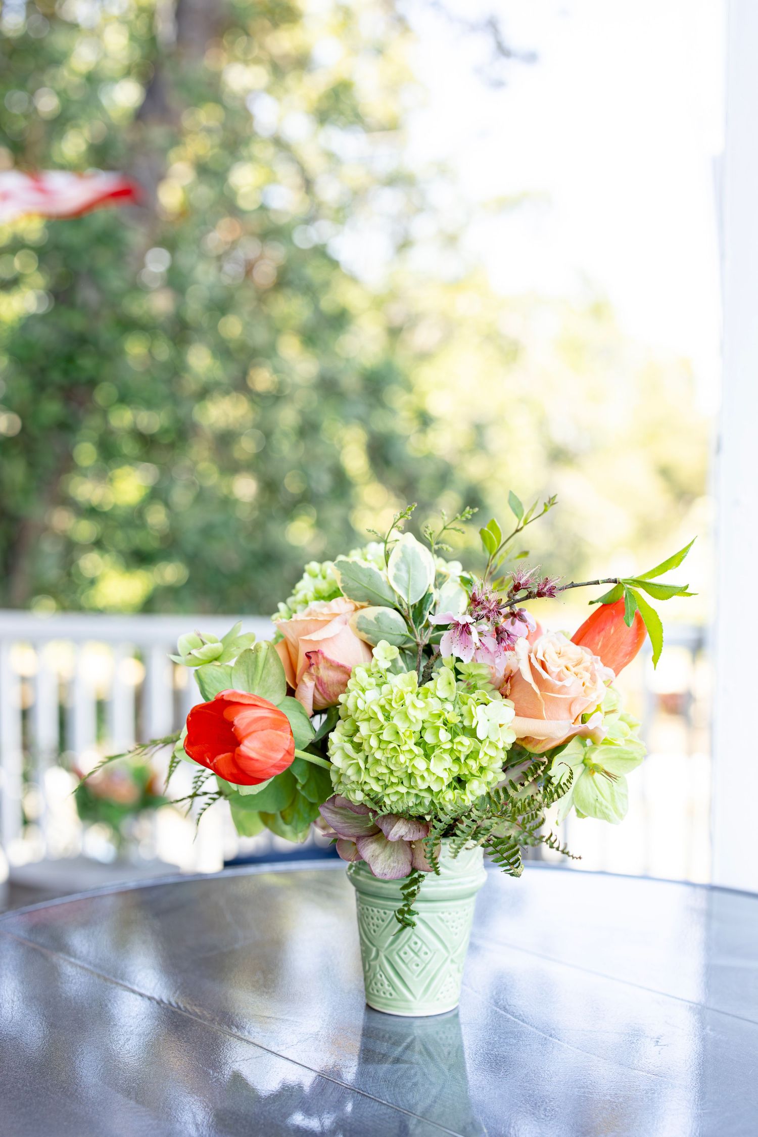 Fresh floral arrangement with red tulips, peach roses, and green hydrangeas in a mint vase.