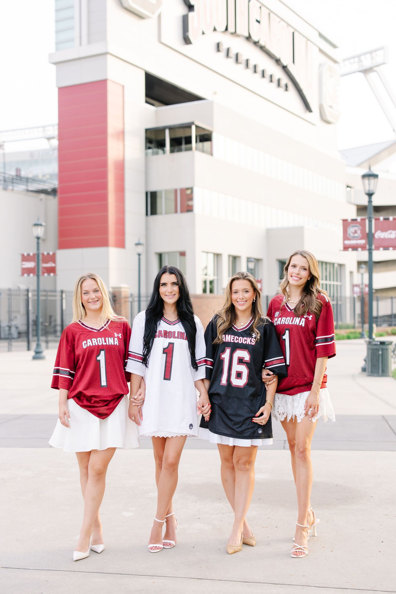 Four smiling women wearing Carolina Gamecocks football jerseys posing outside stadium.