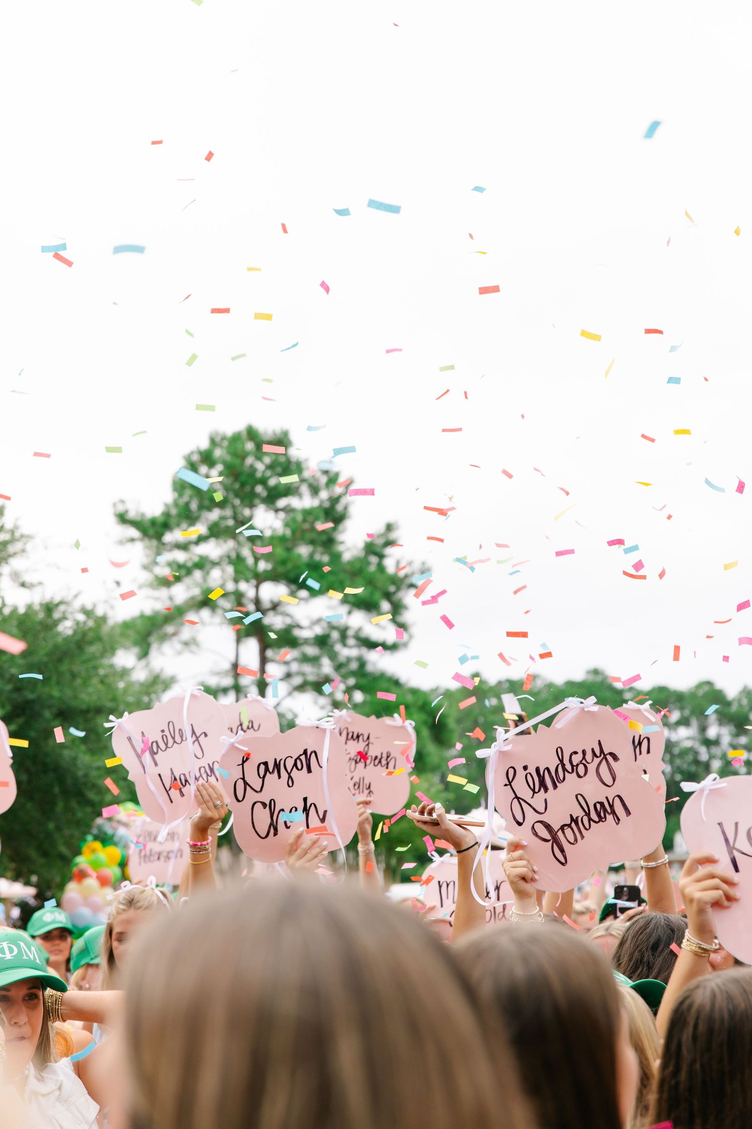 Confetti fills the air as sorority members hold pink bid day signs with new member names written on them.