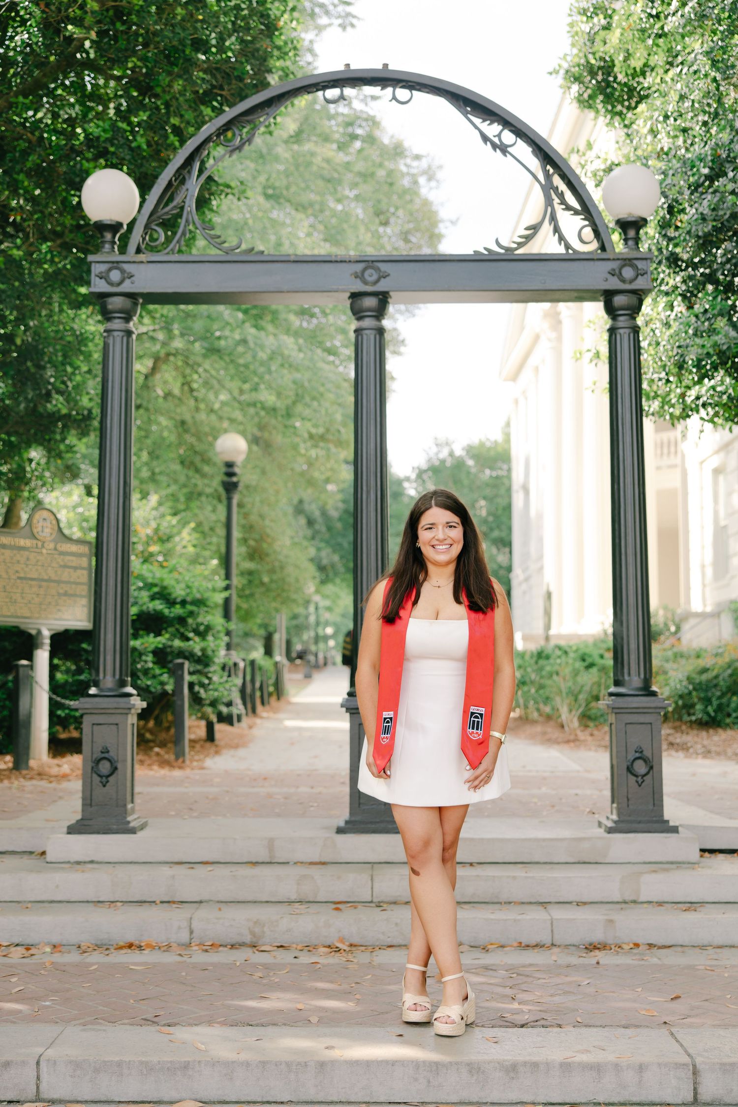 Female graduate in white dress with red stole under university arch.