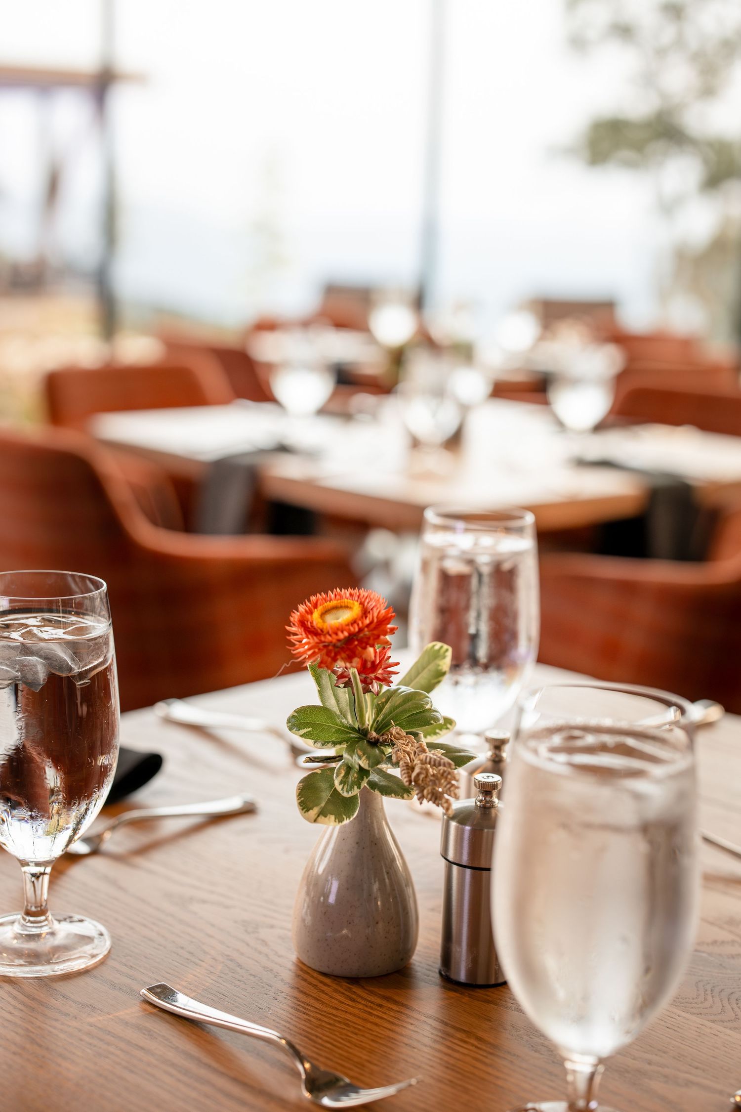 Close-up of a restaurant table setting featuring an orange flower in a white vase with water glasses.