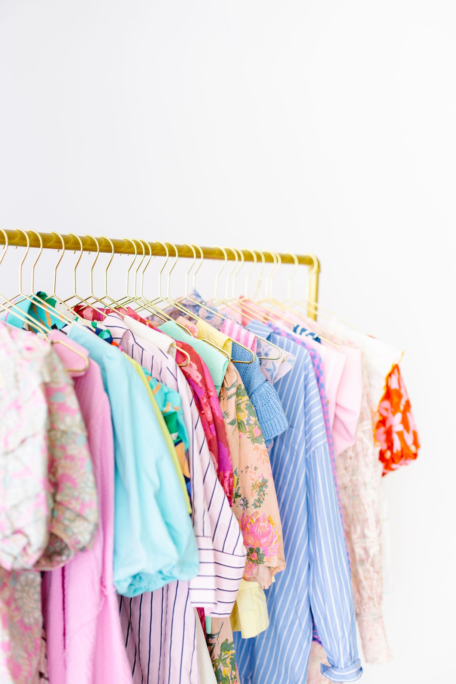 Colorful spring clothing collection hanging on gold rack with pastel floral and striped garments.