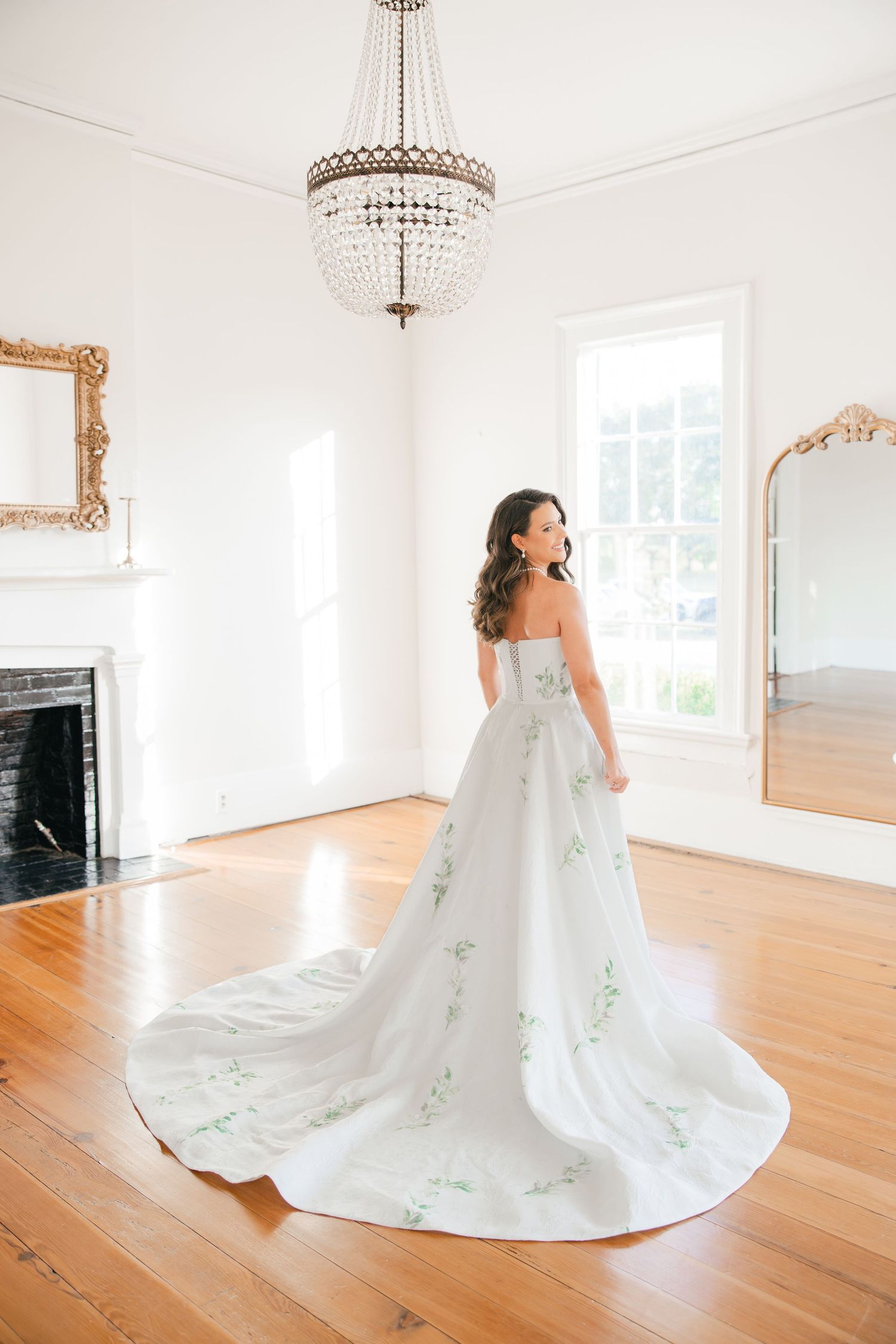 Bride in strapless floral ballgown with train in elegant white room with chandelier.