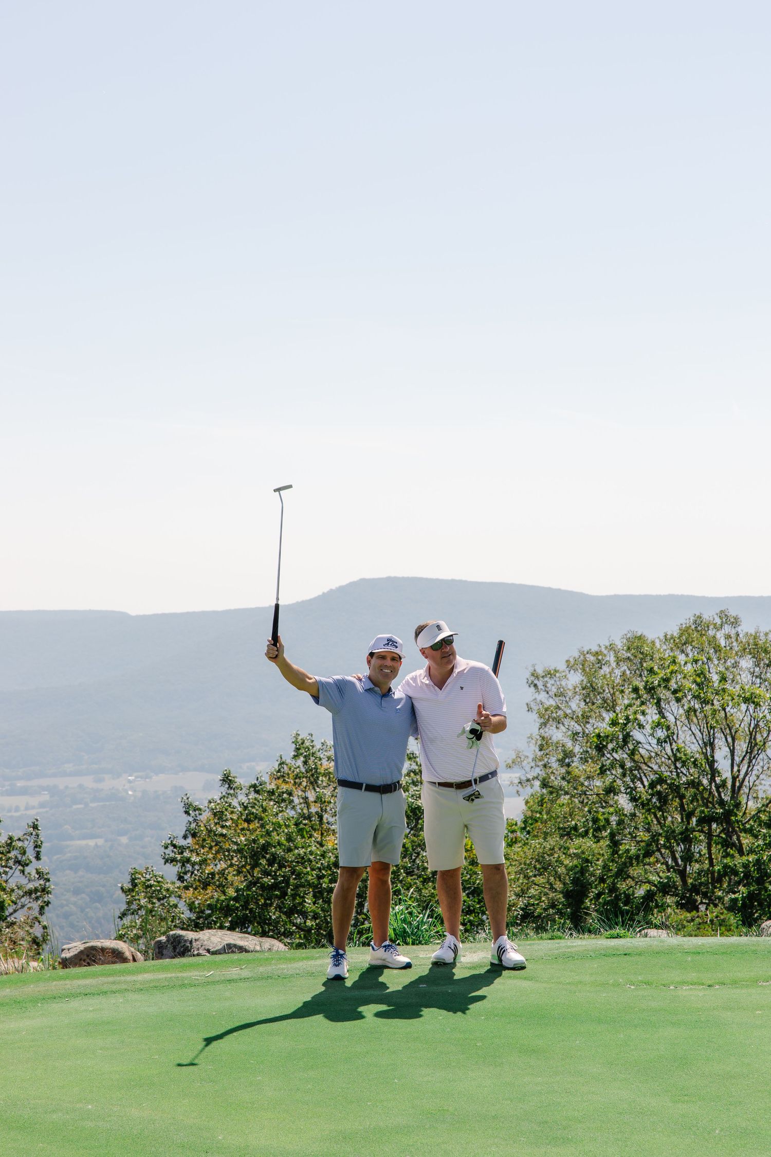 Two golfers celebrating on a green golf course with panoramic mountain views behind them.