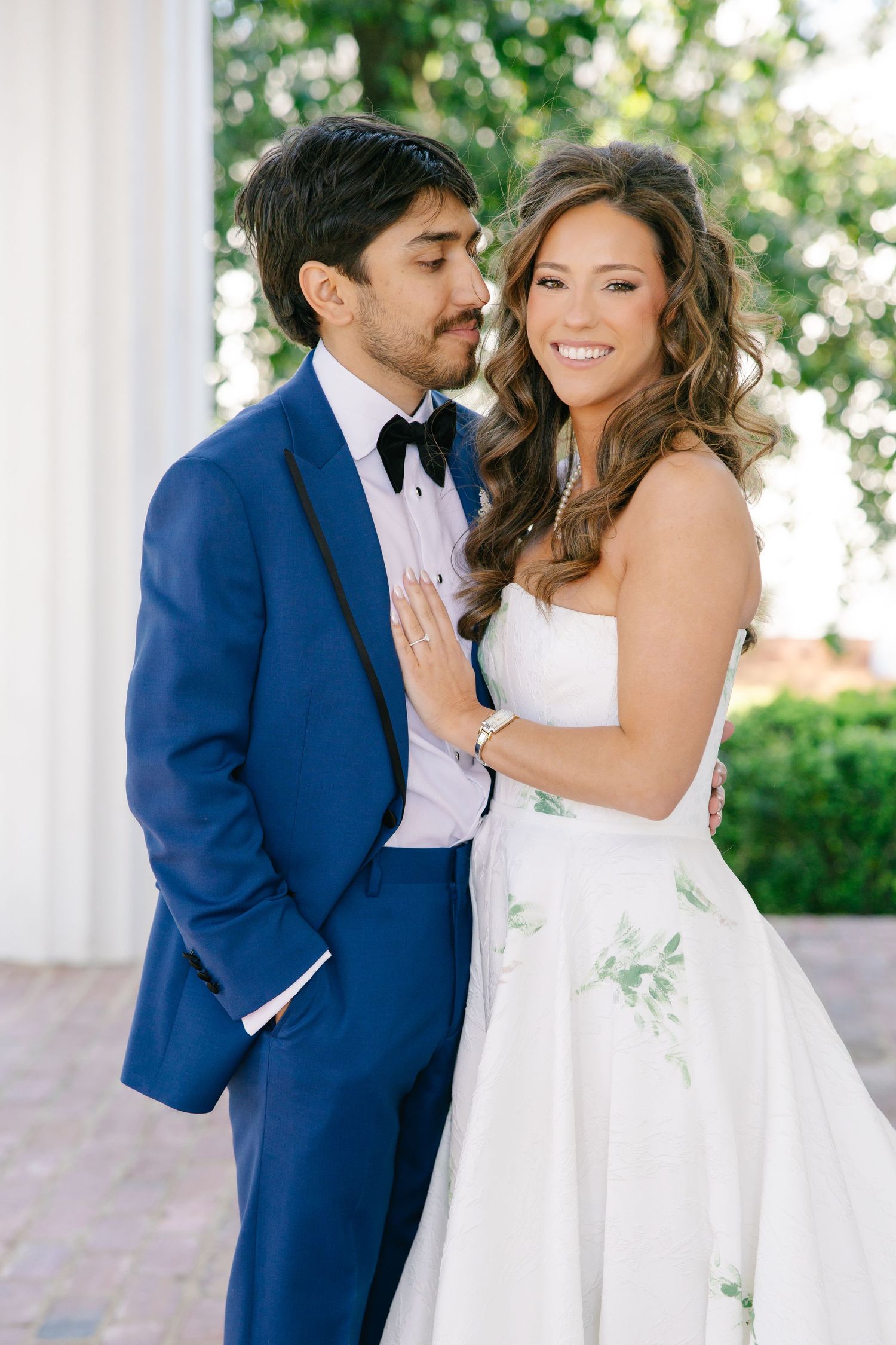 Groom in blue tuxedo kisses bride's cheek as she smiles radiantly in her strapless floral embroidered wedding gown.
