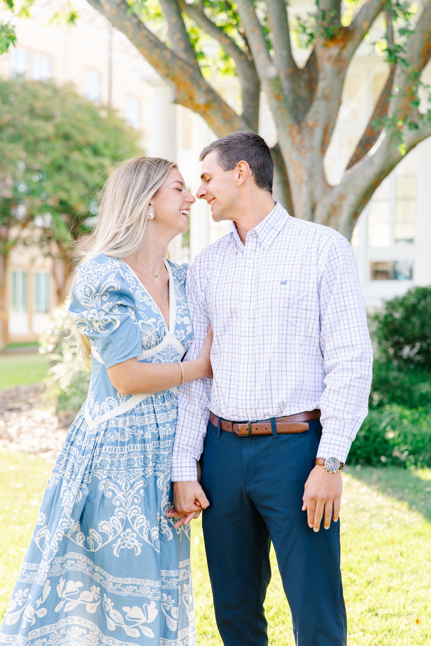 Happy couple in love gazing at each other outdoors beneath a sunlit tree in garden setting.