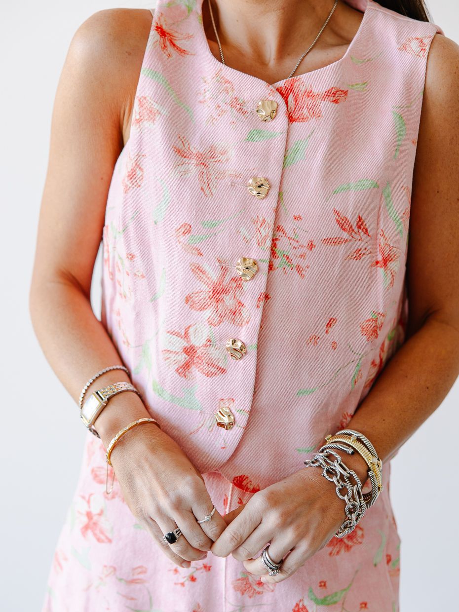Close-up of a pink floral sleeveless dress with gold buttons and layered bracelets and rings on the model.