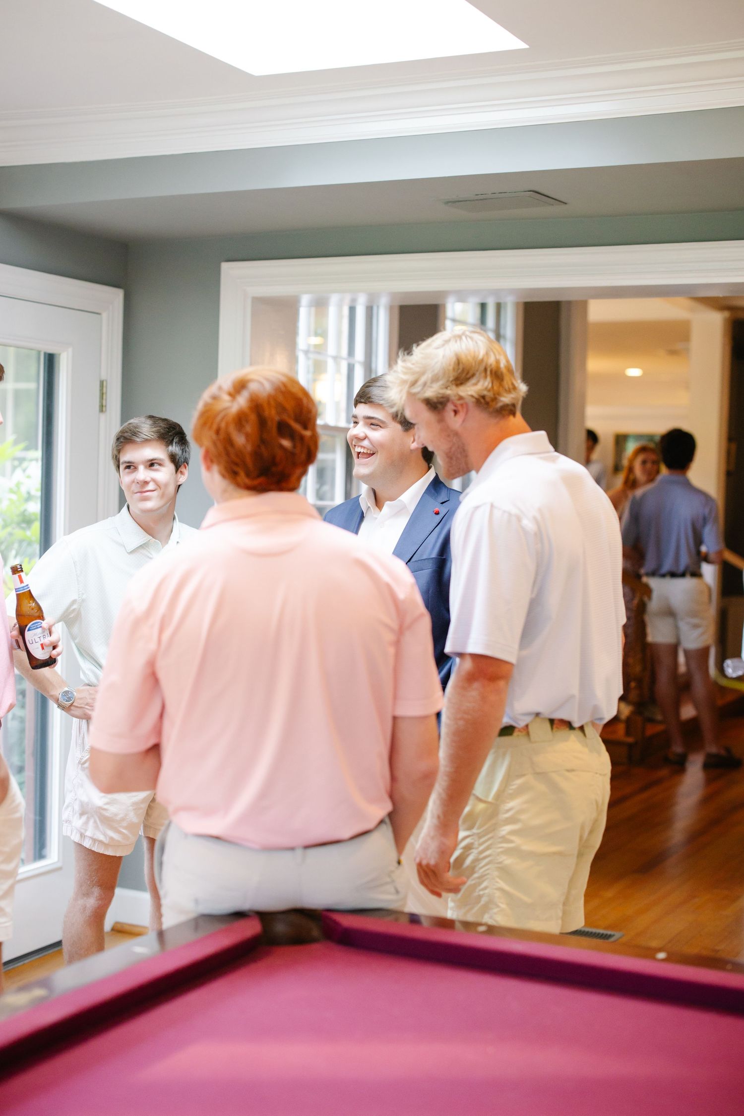 Group of young men in casual preppy attire chatting and laughing near a pool table indoors.