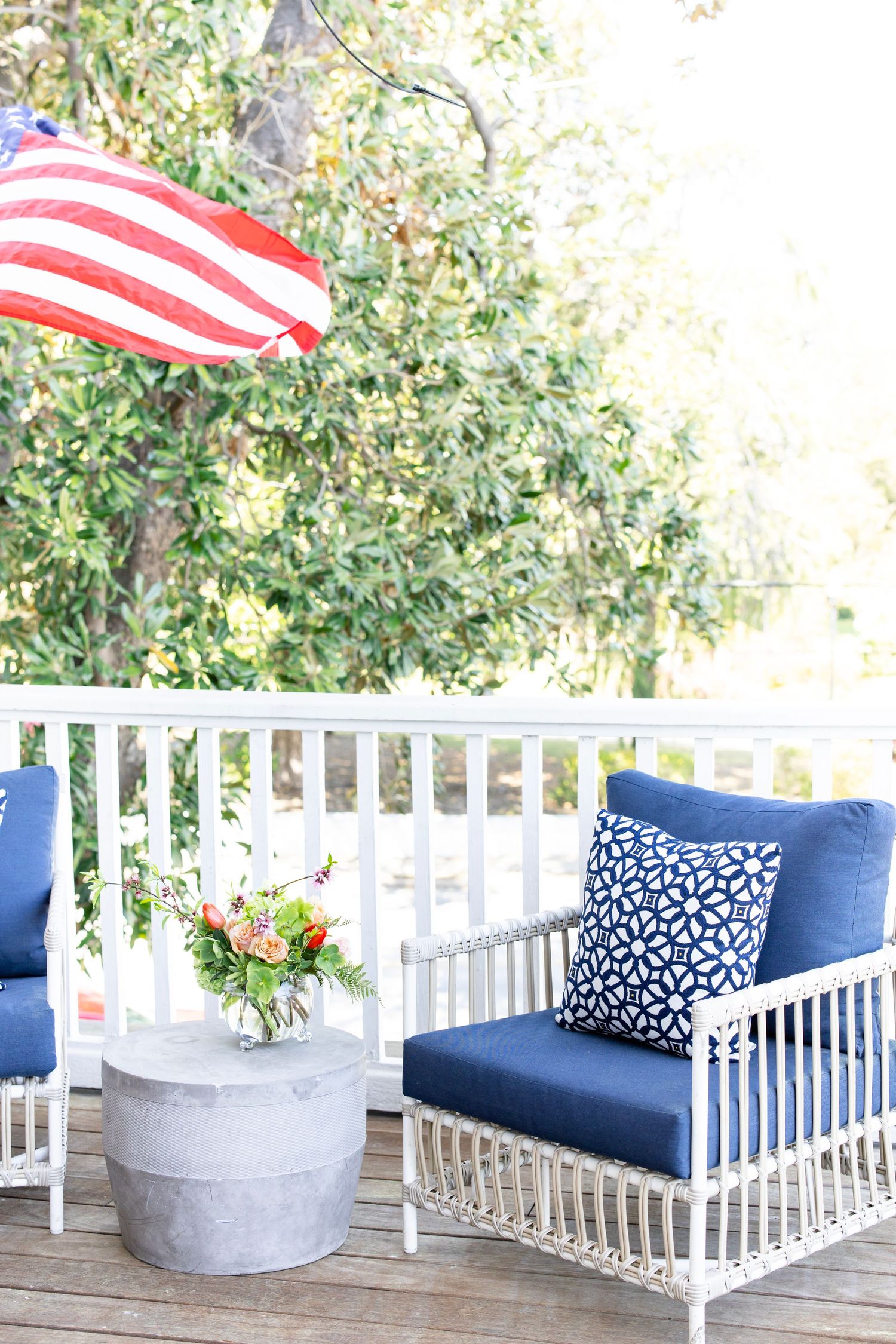 White wicker patio chairs with navy blue cushions on a porch with an American flag.