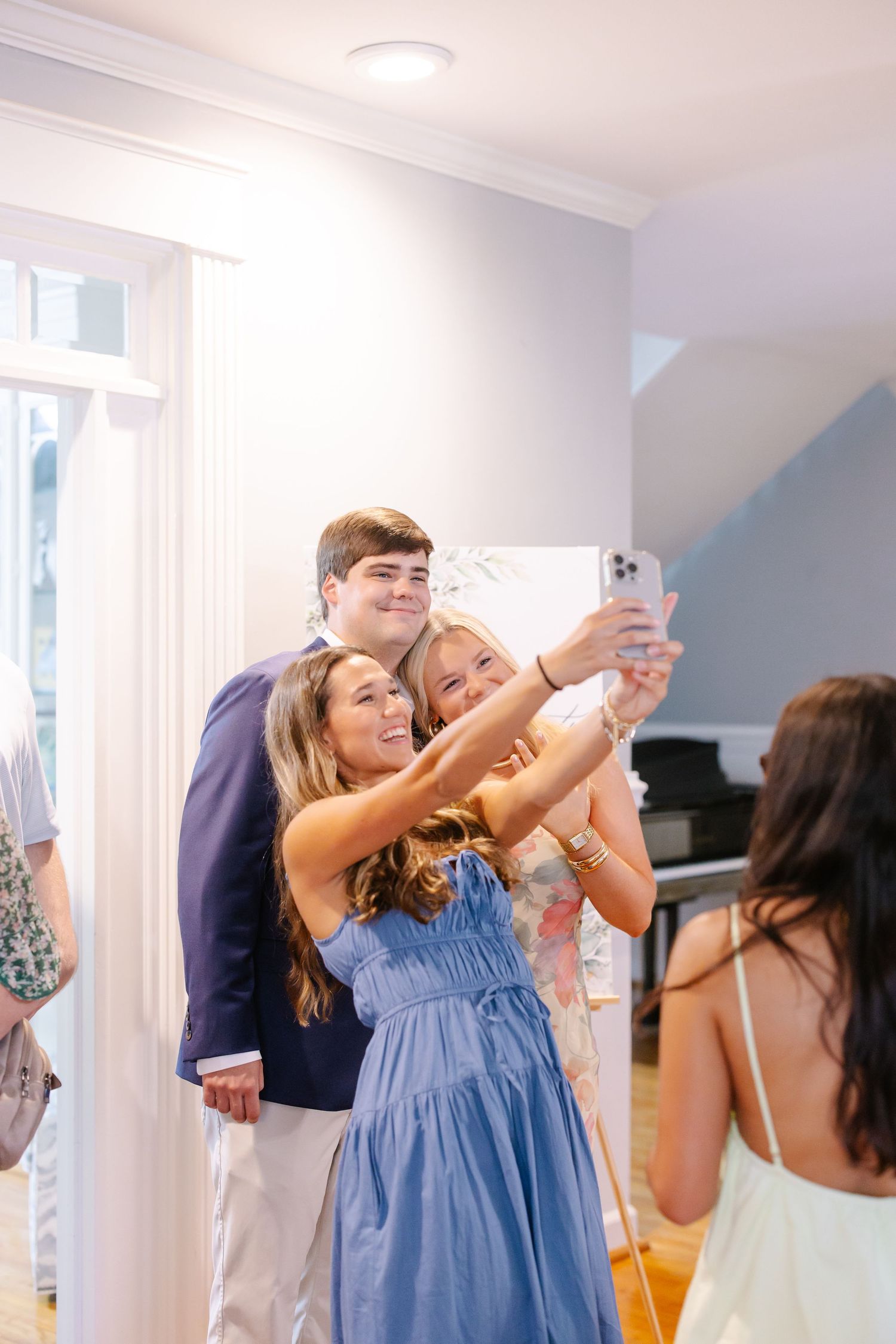 Three friends posing for a selfie with a young man at a bright indoor social celebration event.