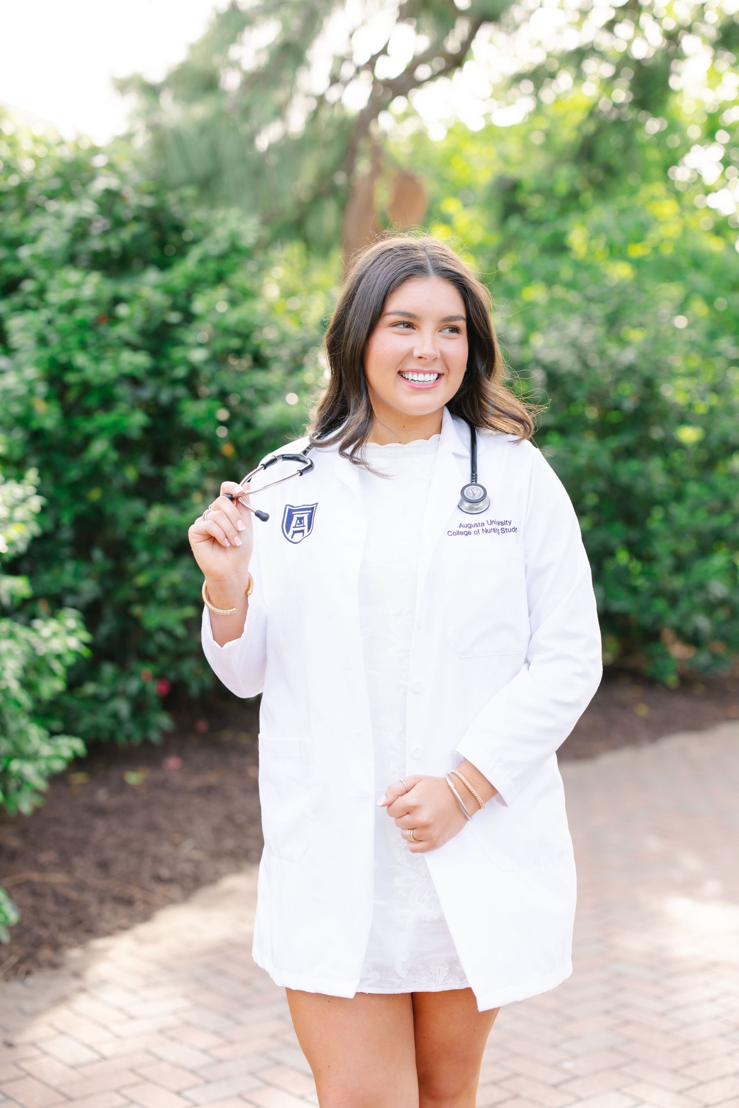 Smiling nursing student in white lab coat with stethoscope and Augusta University emblem outdoors.